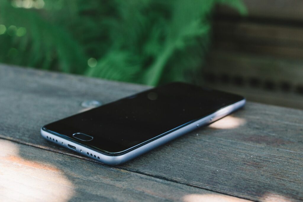 A smartphone lying face up with a dark screen on a wooden table outdoors