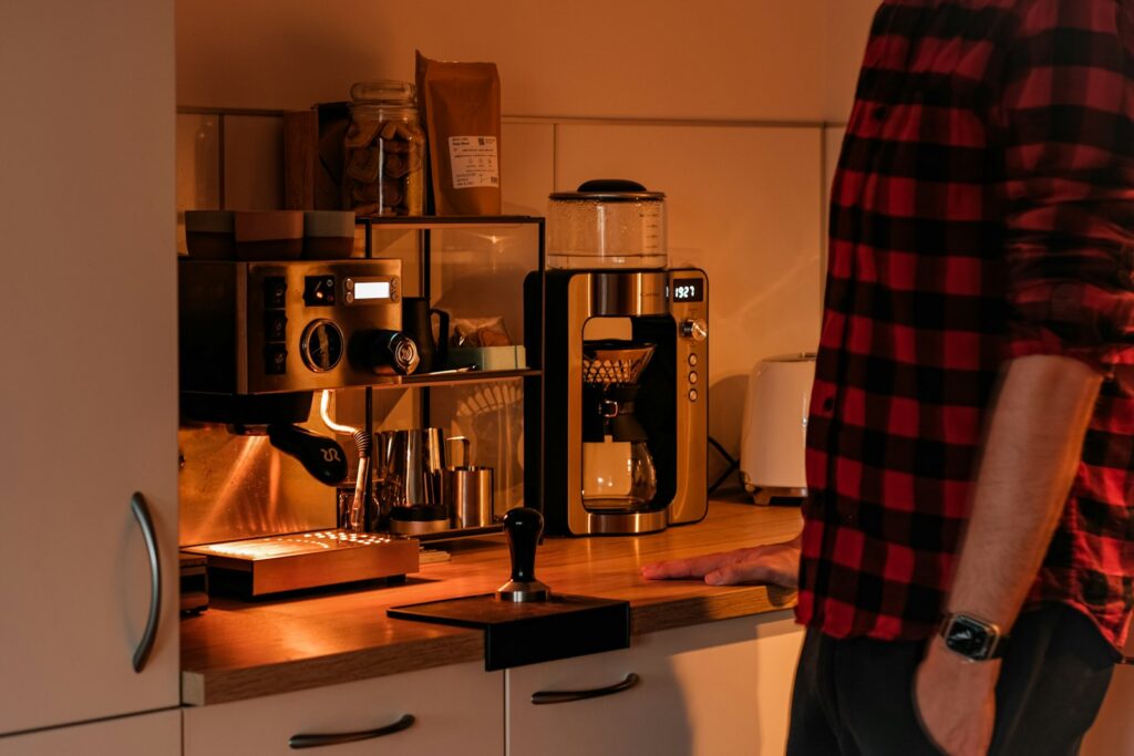 A man standing at a kitchen counter next to a coffee maker and grinder