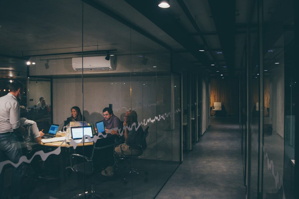 A small team meeting in a glass-walled office room in the evening