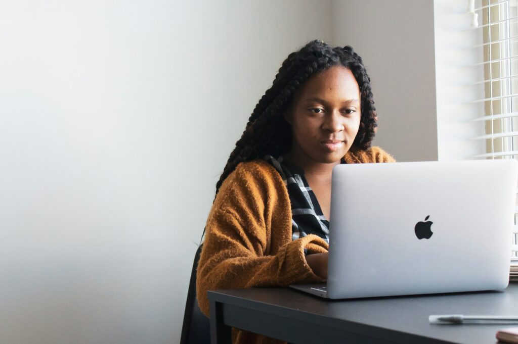 A woman working with focus on a laptop at a desk by a window