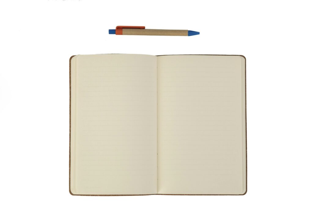 An open blank notebook with lined pages and a pen above it on a white background